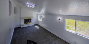 Unfurnished living room with plenty of natural light, a textured ceiling, a brick fireplace, and dark carpet