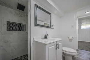 Bathroom featuring tiled shower, wood-type flooring, toilet, and vanity