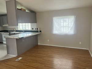 Kitchen featuring gas range gas stove, a kitchen breakfast bar, kitchen peninsula, gray cabinets, and light wood-type flooring