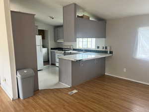 Kitchen with vaulted ceiling, white appliances, a breakfast bar area, and gray cabinetry