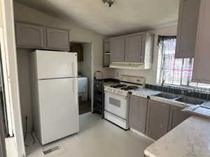 Kitchen with white appliances, a textured ceiling, sink, vaulted ceiling, and washer / clothes dryer