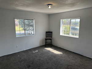 Empty room with a textured ceiling and dark colored carpet