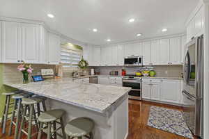 Kitchen with white cabinets, appliances with stainless steel finishes, light stone counters, and kitchen peninsula