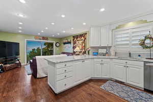 Kitchen with dark wood-type flooring, kitchen peninsula, stainless steel dishwasher, and sink