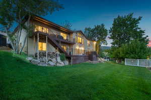 Back house at dusk featuring a lawn and a deck