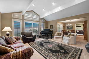 Living room featuring beamed ceiling, high vaulted ceiling, light tile patterned floors, and a notable chandelier