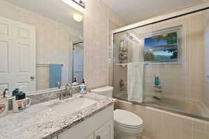 Full bathroom with combined bath / shower with glass door, vanity, and toilet