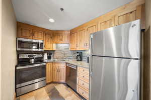 Kitchen featuring appliances with stainless steel finishes, light stone countertops, decorative backsplash, and sink