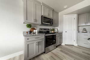 Kitchen featuring gray cabinetry, light wood-type flooring, light stone countertops, and appliances with stainless steel finishes