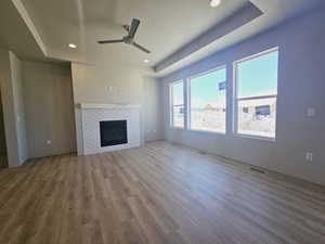 Unfurnished living room featuring a raised ceiling, ceiling fan, a tiled fireplace, and hardwood / wood-style floors