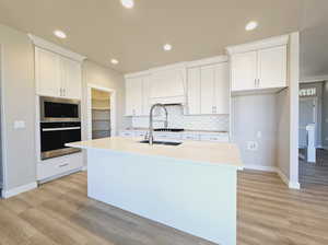 Kitchen featuring appliances with stainless steel finishes, white cabinetry, light hardwood / wood-style flooring, and an island with sink