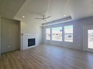 Unfurnished living room featuring a textured ceiling, a raised ceiling, a fireplace, hardwood / wood-style floors, and ceiling fan