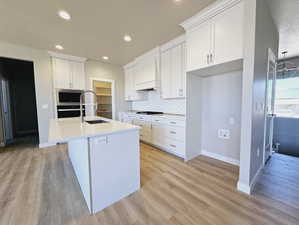 Kitchen featuring custom range hood, a textured ceiling, light hardwood / wood-style flooring, and white cabinets