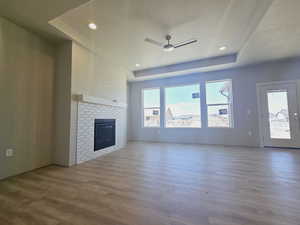 Unfurnished living room featuring a textured ceiling, light hardwood / wood-style flooring, ceiling fan, and a tile fireplace