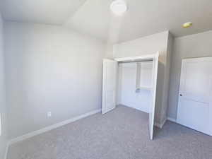 Unfurnished bedroom with carpet, a closet, and vaulted ceiling