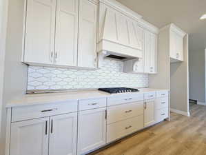 Kitchen featuring light wood-type flooring, white cabinets, light stone countertops, and custom exhaust hood