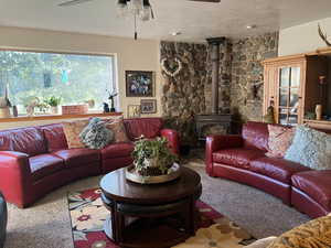 Living room with a wood stove, carpet, ceiling fan, and a textured ceiling