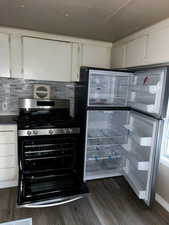 Kitchen with stainless steel range with gas cooktop, white cabinetry, dark wood-type flooring, and fridge