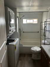 Full bathroom featuring hardwood / wood-style flooring, stacked washer / drying machine, bathing tub / shower combination, vanity, and toilet