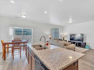 Kitchen with an island with sink, light stone countertops, stainless steel dishwasher, light hardwood / wood-style flooring, and sink