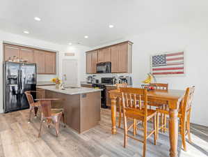 Kitchen with light stone countertops, black appliances, light hardwood / wood-style floors, an island with sink, and sink