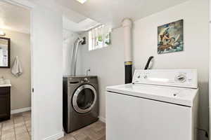 Laundry area with a textured ceiling, separate washer and dryer, and light tile patterned floors