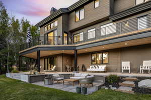 Back house at dusk with a balcony, an outdoor living space, and a patio