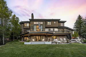 Back house at dusk featuring a lawn, a patio, and a deck