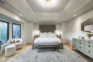 Bedroom with wood-type flooring, a tray ceiling, and a chandelier