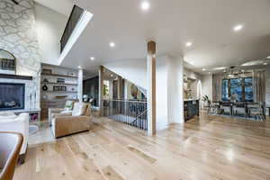 Living room with built in shelves, a stone fireplace, and light wood-type flooring