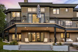 Back house at dusk featuring a balcony, an outdoor hangout area, and a patio area
