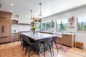 Kitchen with a breakfast bar area, premium appliances, custom exhaust hood, hanging light fixtures, and a center island