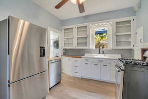 Kitchen with backsplash, stainless steel appliances, light laminate style floors, white cabinetry,