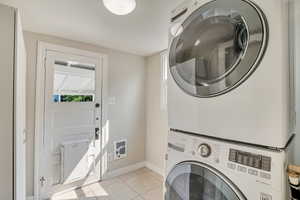 Washroom with stacked washer and clothes dryer and light tile patterned floors