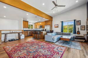 Living room with light wood-type flooring, ceiling fan, and vaulted ceiling with beams