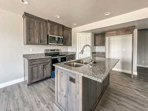 Kitchen featuring appliances with stainless steel finishes, stone countertops, sink, and a center island with sink