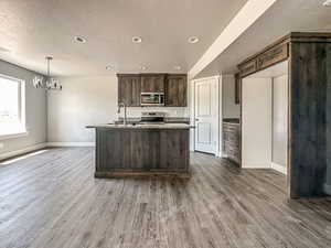 Kitchen featuring a textured ceiling, dark hardwood / wood-style floors, dark brown cabinets, appliances with stainless steel finishes, and light stone counters