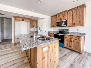 Kitchen featuring appliances with stainless steel finishes, light stone counters, an island with sink, and sink