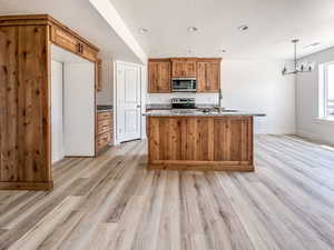 Kitchen with decorative light fixtures, light wood-type flooring, appliances with stainless steel finishes, light stone counters, and sink