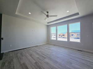 Spare room with ceiling fan, a textured ceiling, a tray ceiling, and hardwood / wood-style floors