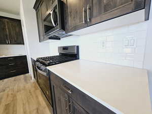 Kitchen with decorative backsplash, dark brown cabinets, light hardwood / wood-style floors, and appliances with stainless steel finishes