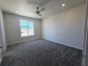 Spare room with ceiling fan, a textured ceiling, and dark colored carpet