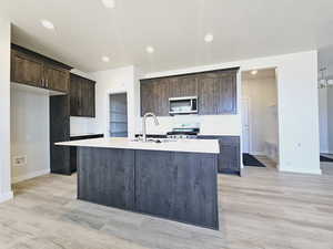 Kitchen with an island with sink, light wood-type flooring, gas range, and sink