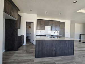 Kitchen with dark brown cabinets, dark hardwood / wood-style flooring, a kitchen island with sink, sink, and decorative backsplash