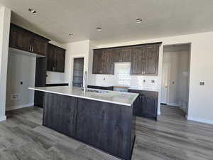 Kitchen featuring a center island with sink, dark wood-type flooring, sink, and a textured ceiling