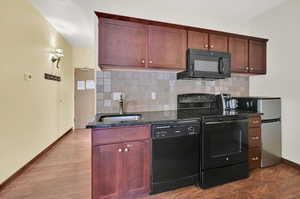 Kitchen featuring dark stone counters, hardwood / wood-style floors, black appliances, sink, and decorative backsplash