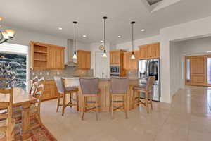 Kitchen featuring decorative light fixtures, stainless steel appliances, wall chimney range hood, open shelves, and backsplash