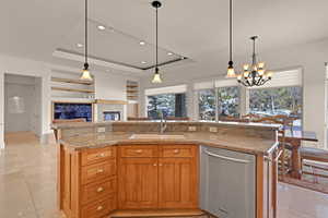 Kitchen with a sink, open floor plan, stainless steel dishwasher, a tray ceiling, and an island with sink