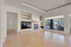 Unfurnished living room featuring built in features, a tray ceiling, light tile patterned floors, recessed lighting, and a tiled fireplace