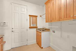 Washroom featuring light tile patterned floors, hookup for a washing machine, cabinet space, a sink, and baseboards